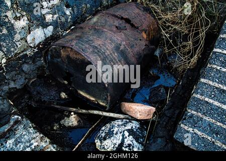 Bidón de metal deteriorado, en balsa de alquitrán y terreno contaminado Foto Stock