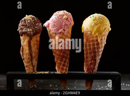 Tre diverse palette di gelato cremoso o gelato cosparse di perle colorate di caramelle o di spolverini in coni di zucchero al wafer con cioccolato, Foto Stock