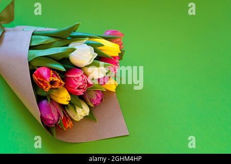 I tulipani multicolore sono avvolti in carta artigianale. Inserire il testo. Bouquet di tulipani. Consegna fiori. Sfondo verde . Tulipano spazio Foto Stock