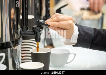 Vista laterale di raccolto anonimo businessperson barman versando caffè caldo aromatico da macchina per caffè in tazza usa e getta mentre serve drink in caffè Foto Stock