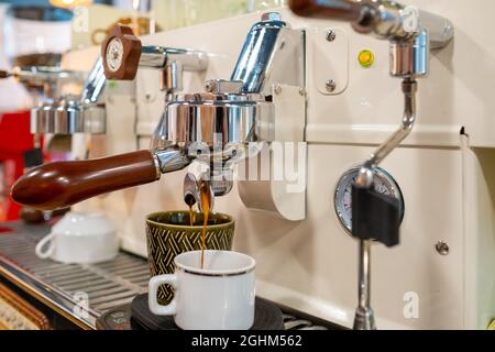 Processo di preparazione dell'espresso in una moderna macchina da caffè con una bevanda calda versata in un paio di tazze in un caffè Foto Stock
