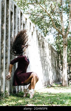 Bella giovane ballerina aggraziata in vestito nero seduta e sulla punta di zoccoli in parco guardando verso l'alto Foto Stock