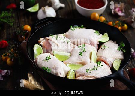 La coscia di pollo cruda non cotta in una padella in ghisa con ingredienti freschi di lime, salsa piccante, timo al limone, peperoni, pomodori e aglio. Foto Stock