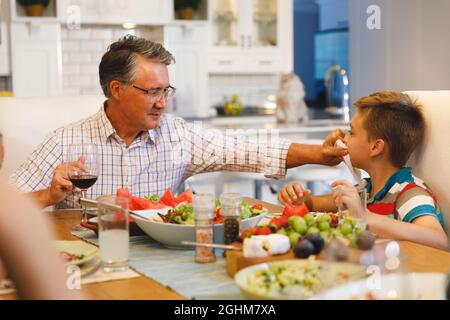 Nonno caucasico strofinando la faccia del nipote mentre si siede a tavola e si cena Foto Stock