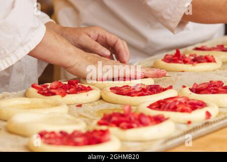 La donna nella foto sta facendo torte di frutta riempite. Mani che riempiono la pasta di lievito con fragole. Lavoro nel panificio. Foto Stock