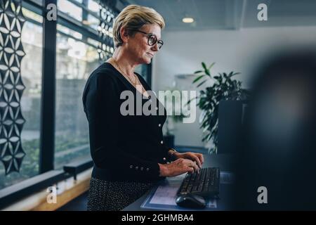 Donna d'affari anziana che lavora in ufficio. Professionista maturo che lavora in ufficio in piedi. Foto Stock