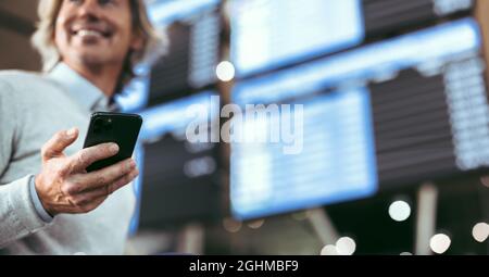 Primo piano di un uomo in piedi al terminal dell'aeroporto con telefono cellulare. Concentratevi sullo smart phone in mano a un viaggiatore maschile in aeroporto. Foto Stock