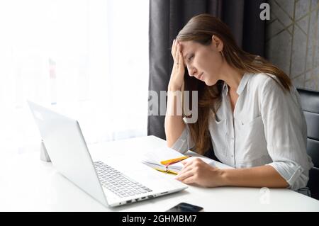 Donna freelance stanca sente lo stress, tiene la fronte e guarda lo schermo del laptop con disperazione, ha problemi finanziari o problemi con il progetto, depressa donna disoccupata non può trovare un lavoro Foto Stock