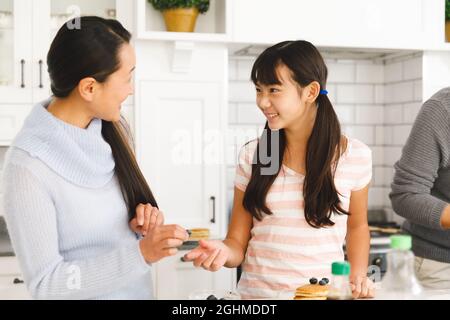 Sorridendo madre e figlia asiatica mentre si prepara la colazione in cucina con il padre Foto Stock