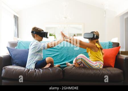 Fratello caucasico e sorella seduti sul divano e utilizzando cuffie vr in salotto Foto Stock