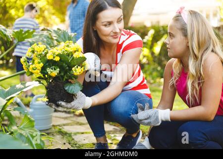 Sorridendo la madre caucasica e la figlia che lavorano in giardino indossando guanti e parlando Foto Stock