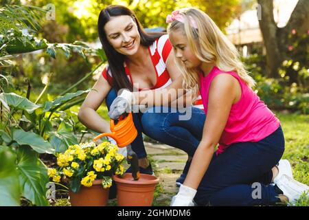 Sorridendo la madre caucasica e la figlia che lavorano in giardino indossando guanti e parlando Foto Stock