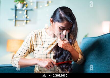 Giovane ragazza indiana sul divano pettinando i suoi capelli lunghi - concetto di donna che si prepara e rituali quotidiani. Foto Stock