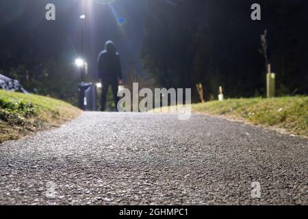 Angolo basso di una misteriosa figura con cappuccio che si trova sotto una luce stradale, nella notte estiva. REGNO UNITO Foto Stock