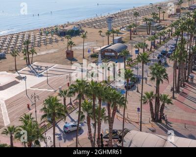 Vista dall'alto sul lungomare di Finikoudes con palme vicino alla spiaggia di sabbia centrale con lettini e sole che splende sull'acqua blu in una giornata di sole. Foto Stock