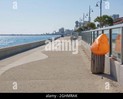 Lungo e vuoto Piale Pasha passeggiata in cemento lungo il mare mediterraneo con aeroplano che scende all'aeroporto di Larnaca. Soffio in plastica arancione. Foto Stock