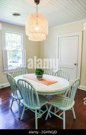 Una piccola sala da pranzo con un'illuminazione in rattan di tendenza e un tavolo da pranzo dipinto di blu Foto Stock