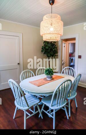 Una piccola sala da pranzo con un'illuminazione in rattan di tendenza e un tavolo da pranzo dipinto di blu Foto Stock