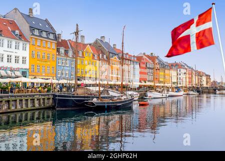 Nyhavn, Copenaghen, Danimarca - 7 settembre 2021 - una bandiera danese vola nel vento con una vista di Nyhavn, Copenaghen sullo sfondo. Foto Stock