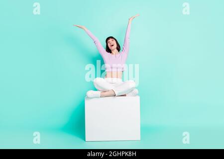 Full length body size foto donna seduta in studio mantenendo le mani su overjoyed isolato vibrante sfondo di colore turchese Foto Stock