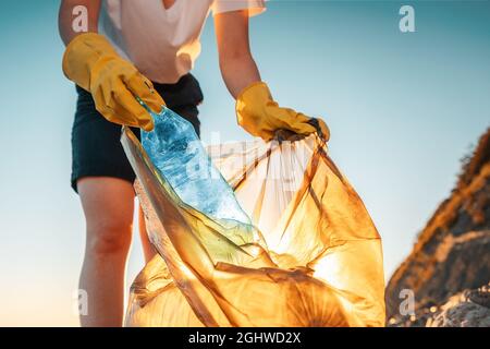 Giorno della terra. Un'attivista femminile mette una bottiglia di plastica in un sacchetto per rifiuti. Primo piano. Il concetto di conservazione ambientale e di pulizia delle zone costiere. Foto Stock