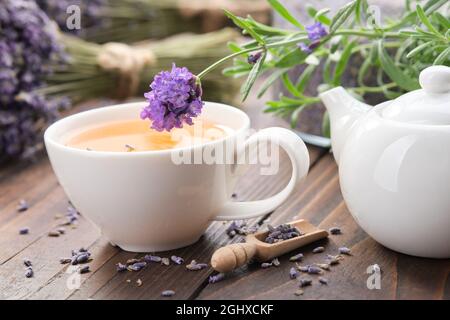 Sana tazza di tè alle erbe di lavanda, bollitore per tè, fiori freschi e secchi di lavanda su tavola di legno. Foto Stock