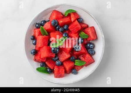 Insalata di melone e mirtillo con menta in un piatto su sfondo bianco. Vista dall'alto. Rinfrescante cibo estivo Foto Stock