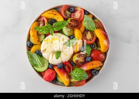 Deliziosa insalata estiva con burrata, pesche alla griglia, pomodori, mirtilli, cetrioli, olio d'oliva e basilico. Vista dall'alto. Dieta sana Foto Stock