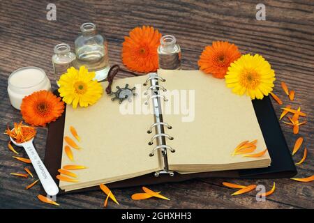 Calendula fiori usati in medicina di erbe con il vecchio taccuino, unguento e bottiglie di olio. Usato nella cura della pelle per guarire le ferite, l'acne, l'eczema. Foto Stock