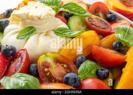 Insalata di burrata con pesche alla griglia, pomodori, mirtilli, cetrioli e basilico. Primo piano. Dieta sana concetto di cibo Foto Stock