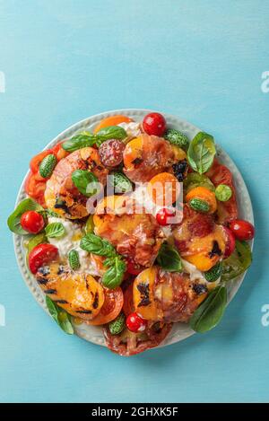 Deliziosa insalata con burrata, pesche alla griglia e prosciutto, burrata, pomodori, cetrioli, olio d'oliva e basilico. Vista dall'alto. Dieta sana f Foto Stock