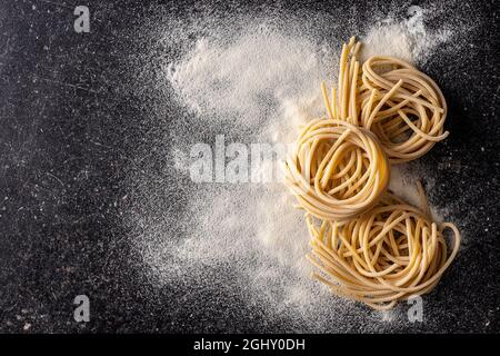 Nido di pasta italiana. Gli spaghetti non cotti nidificano e farina su tavola nera. Vista dall'alto. Foto Stock
