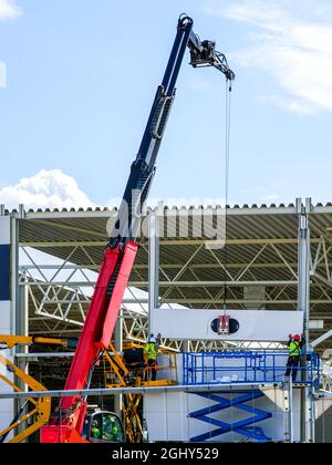 una parete a pannelli sandwich è montata con l'aiuto di una moderna gru telescopica e sollevatori a forbice Foto Stock