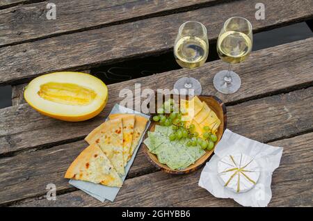 Picnic al molo di legno vicino al lago con cibo, frutta e vino bianco. Picnic per due, romantica attività all'aperto Foto Stock