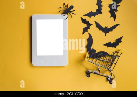 Schermo vuoto del laptop su sfondo giallo con Halloween decor.Paper pipistrelli e ragni scrambled fuori dello spazio del carrello di shopping.Copy. Vendite autunnali Foto Stock