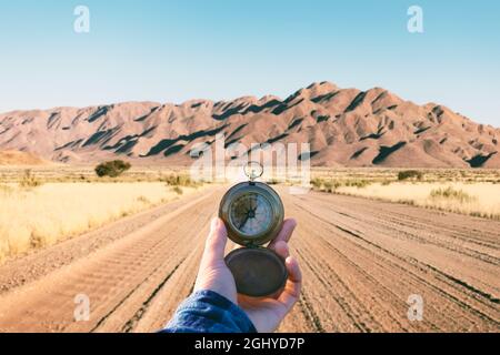 Uomo con vecchio compasso in metallo in mano su strada di ghiaia in Namibia, Africa. Concetto di viaggio. Fotografia di paesaggio Foto Stock