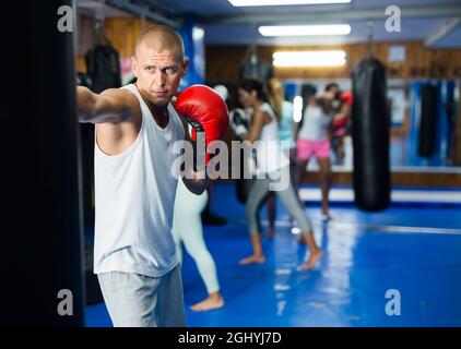 Giovane uomo in guanti da boxe che pratica punzoni su borsa in palestra Foto Stock