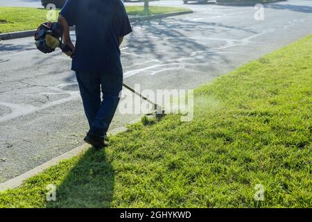 Un tosaerba falcia erba fresca e verde sul prato vicino, un operaio comunale con il tosaerba in mano. Foto Stock