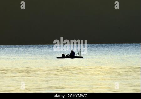 Una silhouette di un uomo che pesca da una barca di gomma nel canale Stewart sulla costa dell'isola di Vancouver British Columbia Canada. Foto Stock