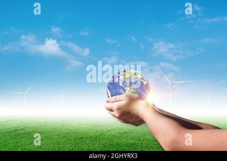 Mani che tengono terra, globo su campo di turbina eolica su sfondo cielo blu. Concetto di ambiente Foto Stock