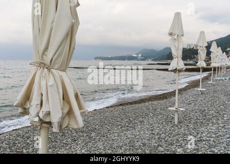 Spiaggia di ciottoli vuota e sedie a sdraio chiuse, nessuna nuotata in mare Foto Stock