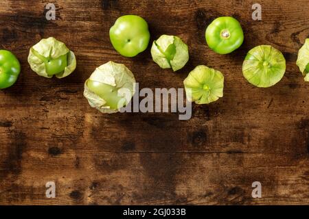 Tomatillos, pomodori verdi, sparati dall'alto con un posto per il testo. Ingrediente alimentare messicano su un sfondo rustico scuro in legno Foto Stock