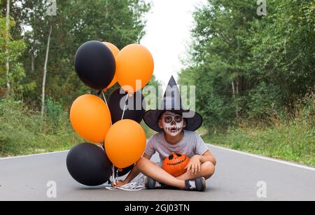 Ragazzo emotivo con trucco tiene zucca e palloncini spooky Foto Stock