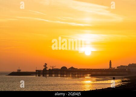 Il sole che sorge in un cielo arancione sopra la silhouette del molo presso la località costiera Kent di Herne Bay. In primo piano la spiaggia e il groynes, wave breakers in legno. Foto Stock