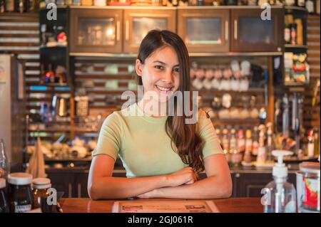 Bella giovane donna asiatica imprenditore di piccola impresa in piedi e sorridente al banco di legno sul posto di lavoro Foto Stock