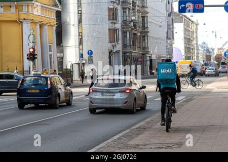 Riga, Lettonia - 7 Aprile, 2021: Corriere Wolt Food in bicicletta con un sacco di merci per strada, consegna veloce di cibo in bicicletta Foto Stock