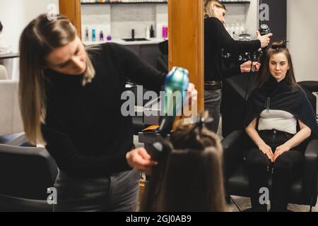 Master donna parrucchiere asciuga i capelli della ragazza con un asciugacapelli dopo il lavaggio in un salone di bellezza. Foto Stock