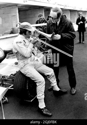 Brands Hatch, Kent: Il pilota di corse Jackie Stewart, scozzese, non sta davvero soffiando la sua tromba - come si può vedere - ma il trombone del bandleader jazz Chris Barber. Jackie Stewart reckons può andare più veloce di qualsiasi altro pilota del Gran Premio sul bagnato, e chris afferma che piove sempre quando si trova al Brand Hatch Racing Circuit. Così nella giornata di prove Chris ha obbligato Jackie girandosi, completo di strumento. Beh, pioveva un po', ma la pratica è stata finalmente abbandonata a causa della fitta nebbia. Non pioveva ieri, ma Jackie vinse ancora la gara dei campioni nella sua Matra-Ford di Formula uno C. Foto Stock