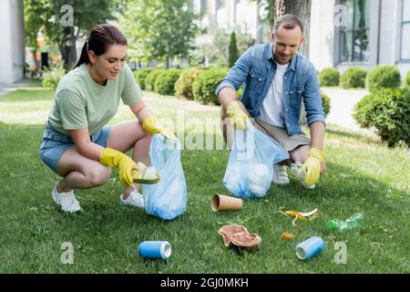 Coppia sorridente in guanti di gomma raccolta rifiuti in borse sul prato Foto Stock