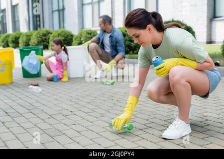 Donna che raccoglie rifiuti da terra vicino alla famiglia sfocata all'aperto Foto Stock